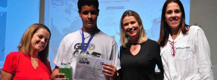 De pé, no palco do Teatro Mario Covas, da esquerda para a direita, a supervisora Karina Soares, o vencedor, Kauan, que segura o prêmio com a mão direita e o certificado com a mão esquerda com a medalha no pescoço, a secretária Márcia Paiva e a coordenadora do Apoio Pedagógico, Alessandra Ciaca.