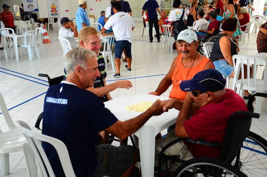 Idosos na mesa dão as mãos após rodada de dominó